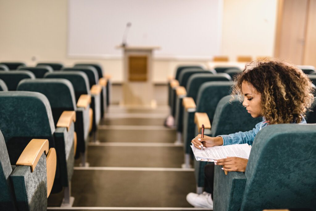 Female student reading a lecture from papers in an empty lecture hall.