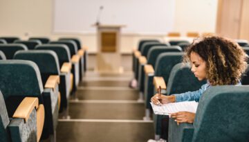 African American female student reading a lecture from papers in an empty lecture hall.