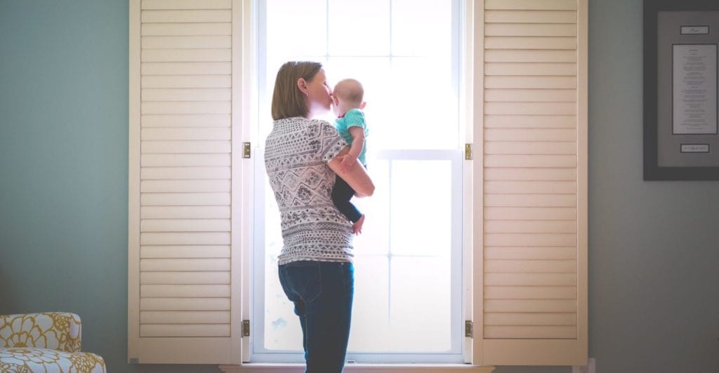 Mother with child looking at window and kissing baby