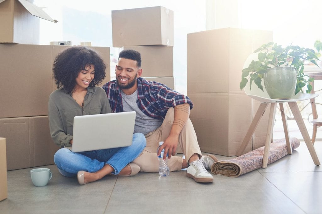 young couple using a laptop in living room with boxes