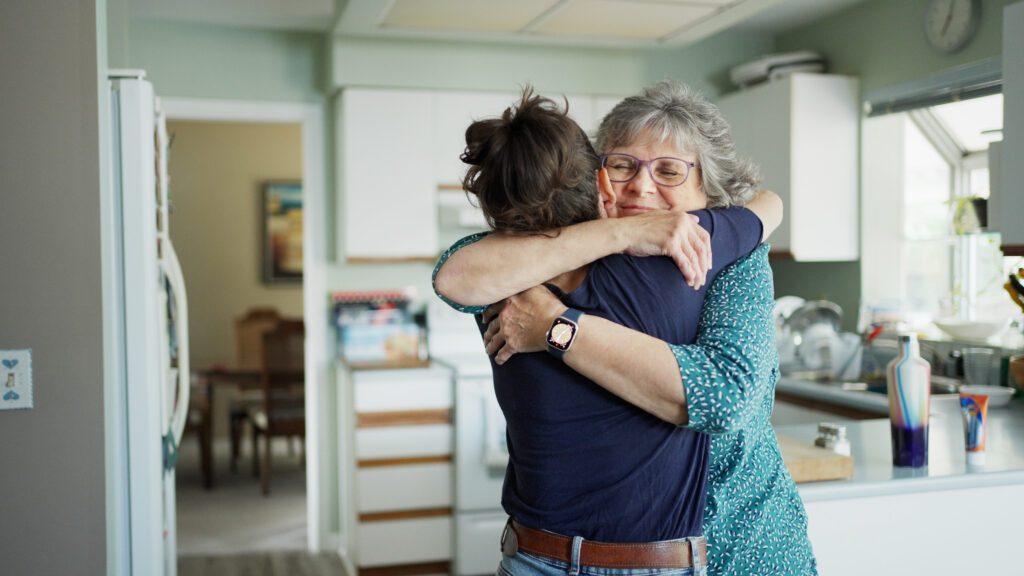 Over the shoulder view of a smiling mature woman giving her adult daughter a hug after arriving home for a visit