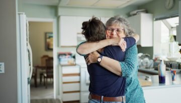 Over the shoulder view of a smiling mature woman giving her adult daughter a hug after arriving home for a visit