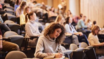 Female college student writing an exam during a class at lecture hall.