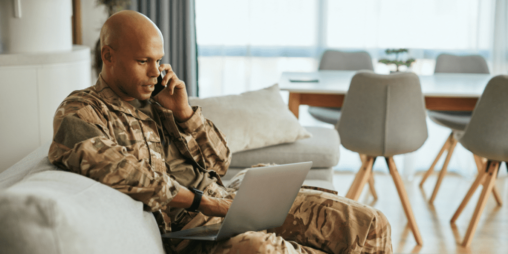 Young black male military veteran sitting on the phone with laptop.