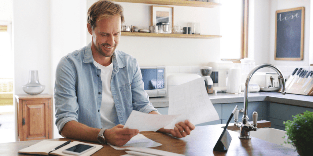 Young adult man looking at student loans and tax paperwork in kitchen.