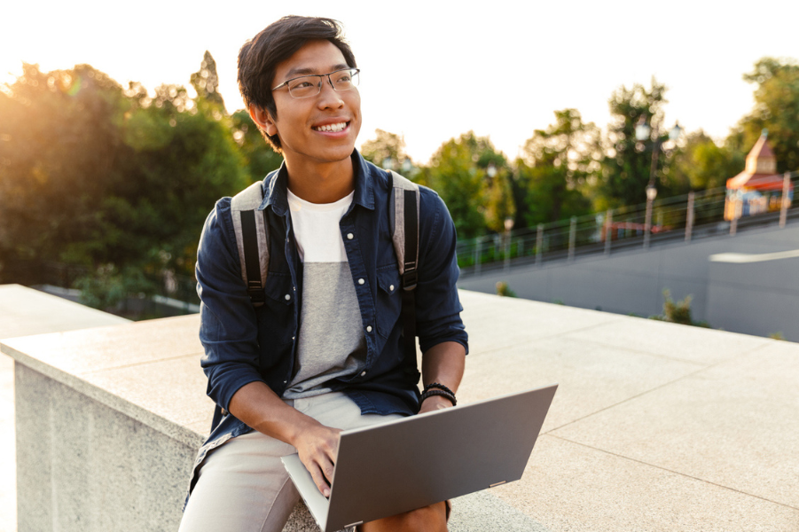 Young Asian college student sitting with laptop on college campus.