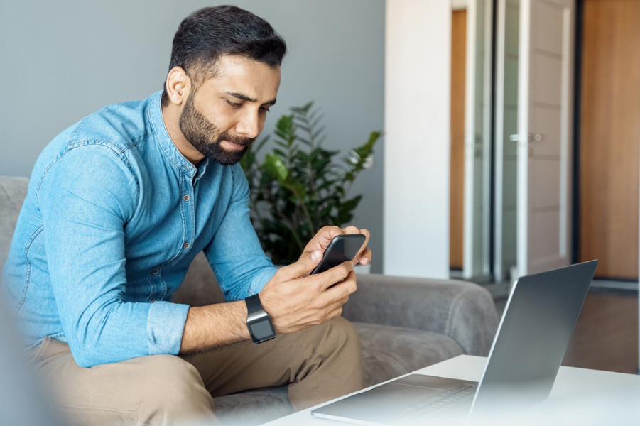 Man sitting on laptop with phone looking at student loan refinancing.