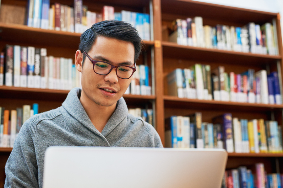 Asian male college student researching on his laptop.