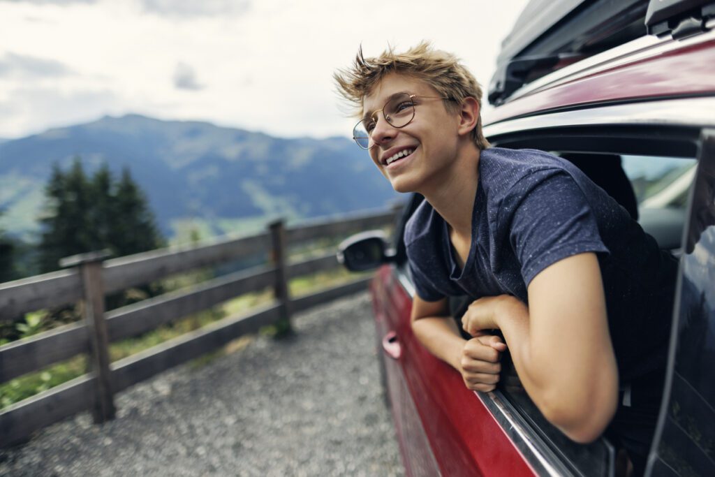 Teenage boy leaning out car window at mountain view