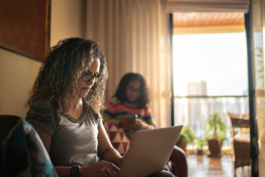 Mother sitting with laptop on couch with daughter sitting next to her.