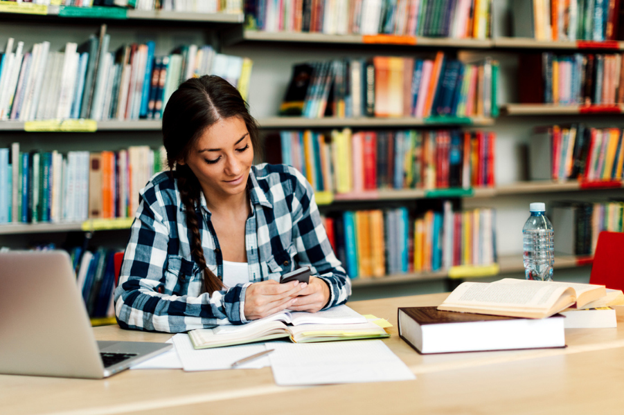 Female college student in the library looking at her phone.