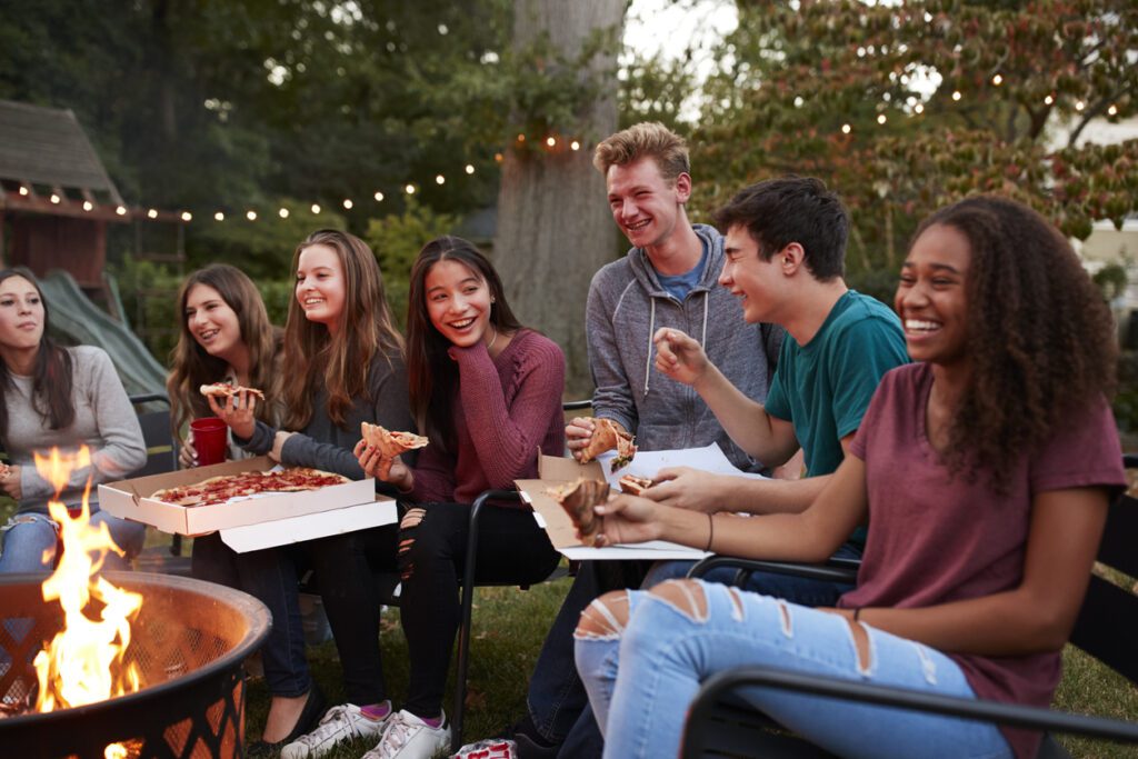 Teenagers at a fire pit eating take-away pizzas