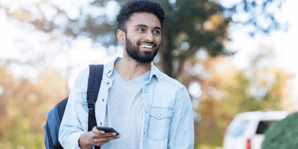 Young college male walking around college campus holding phone.