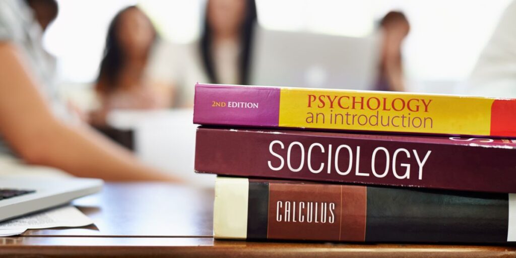 Three textbooks sitting with students who are curious how to pay for college books.