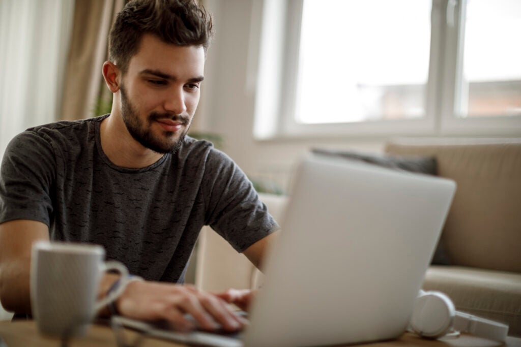 male college student changing student loan repayment plan on laptop.