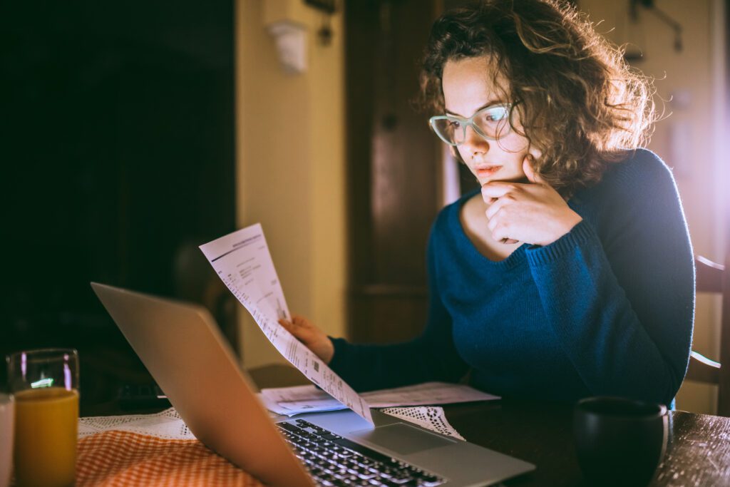 Young brunette curly female reading her bill papers, looking stressed