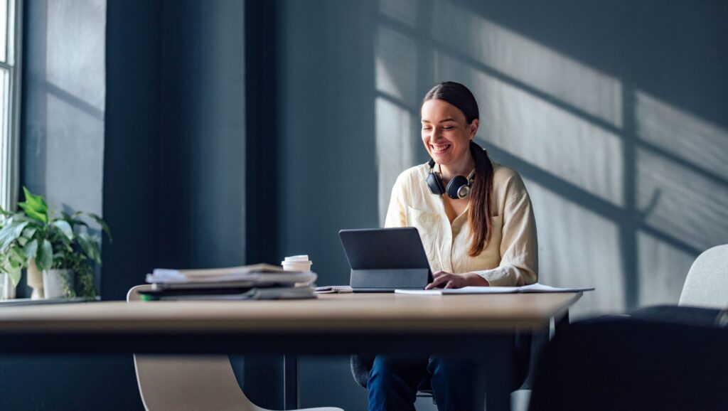 Happy woman sitting at desk with tablet