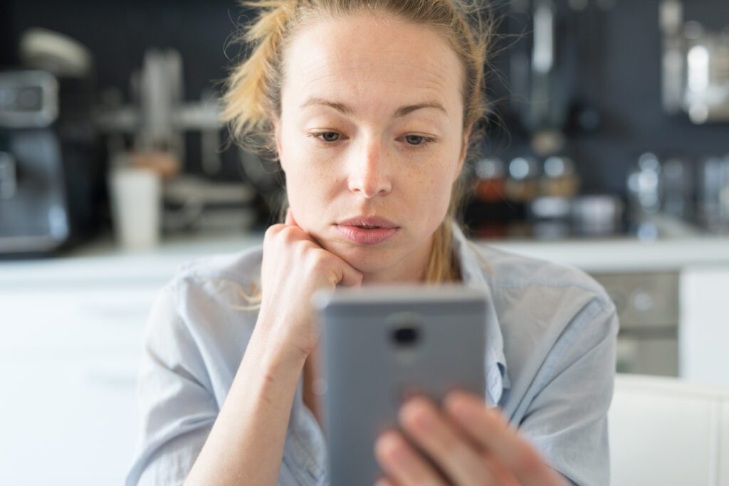 Young woman reviewing news on phone in kitchen