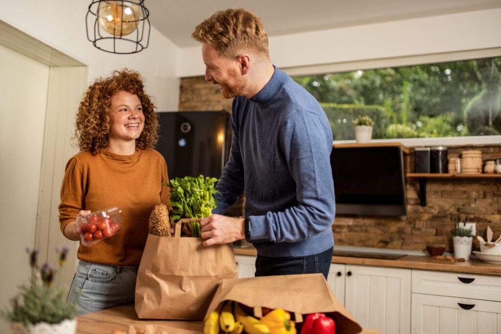 Happy young couple unpacking groceries in the kitchen.