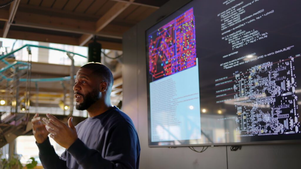 Black man conducting a seminar on Python computer coding in an open plan work arena