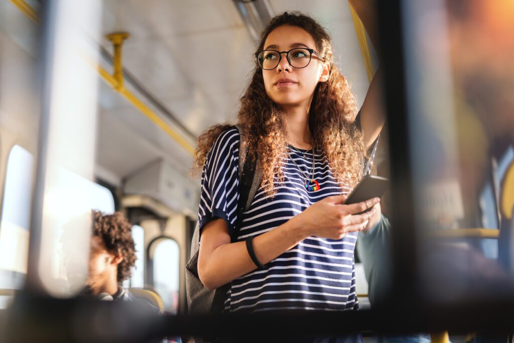 Student age girl using smartphone while standing on bus